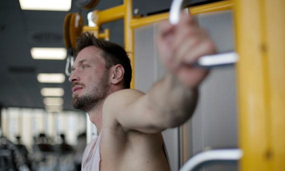 Muscular man exercising on gym equipment, demonstrating strength and focus in a fitness environment.